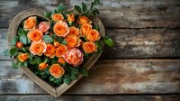 Orange and peach roses arranged in rustic wooden heart-shaped box against weathered wood background, romantic floral composition with green leaves.