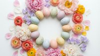 Easter wreath with pastel colored eggs, ranunculus flowers, peonies and petals arranged in circle on white background for spring holiday decoration.