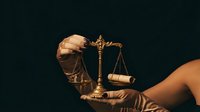 Golden scales of justice held in gloved hands against dark background symbolizing law, legal system, and courtroom proceedings for professional use.