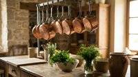 Copper pots hanging from rack in rustic kitchen with herbs and wooden countertop creating warm cooking atmosphere for culinary design projects.