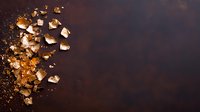 Scattered sea salt crystals and crumbs on dark rustic background with dramatic lighting and copy space, overhead view for food photography and culinary designs.