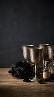 Vintage brass goblets with dark roses and poison bottle on wooden table against black textured background for gothic themed designs and Halloween concepts.