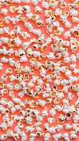Fresh popped popcorn scattered on vibrant coral background. Snack food texture pattern for movie night, cinema, entertainment designs.