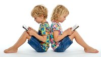 Two young blonde children sitting back to back using smartphones on white background, digital technology and screen time concept for kids.