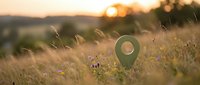 Green location pin marker in golden sunset meadow with purple wildflowers and warm bokeh light creating peaceful navigation concept for travel apps.