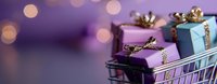 Shopping cart filled with small wrapped gift boxes in purple and blue with gold ribbons against blurred purple bokeh background, holiday retail concept.