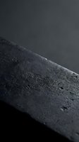 Dark textured stone surface with rough granular finish and dramatic lighting creating depth and shadow for modern design backgrounds.