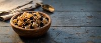 Healthy trail mix with nuts, dried fruits and seeds in wooden bowl on rustic blue table for snacking and outdoor adventures.