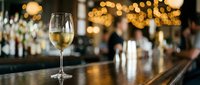 Glass of white wine on elegant bar counter with warm bokeh lights creating sophisticated restaurant atmosphere for dining and entertainment.