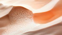 Swirling cream and coffee blend creating smooth waves and bubbles in warm orange and white tones, macro photography showing rich texture and movement.