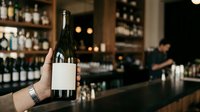 Sommelier or bartender holding wine bottle with blank label in upscale bar or restaurant setting, showcasing premium beverage service and hospitality industry.