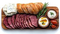 Sliced roast beef and blue cheese platter served on wooden board with fresh rosemary, cherry tomatoes and dipping sauces, arranged for appetizer presentation.