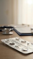 Blister pack of white pills on wooden desk with stethoscope and clipboard in medical office background for healthcare and pharmaceutical concepts.