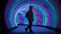Person walking through illuminated LED tunnel with vibrant purple and blue neon lights creating futuristic digital corridor for technology concepts.