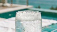 Refreshing glass of sparkling water with bubbles by swimming pool on sunny day. Hydration drink for summer relaxation and wellness lifestyle.