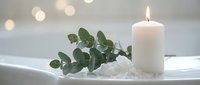 Spa relaxation scene with lit white candle, eucalyptus branch and sea salt in bathtub creating peaceful wellness atmosphere for self-care rituals.