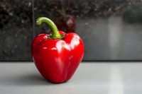 Fresh red bell pepper with green stem on kitchen counter ready for cooking and meal preparation in modern home setting.