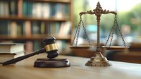 Wooden judge gavel and vintage brass scales of justice on desk in law office, with blurred bookshelf background, symbolizing legal system and judicial process.