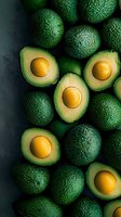 Fresh ripe avocados, whole and halved showing golden pits against dark background, arranged in artistic food composition for healthy eating concept.