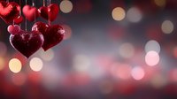 Sparkling red heart decorations hanging against blurred bokeh background with romantic mood lighting, creating festive Valentine's Day atmosphere.
