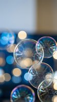 Floating soap bubbles with rainbow reflections against blurred bokeh lights background creating dreamy atmospheric scene for relaxation concepts.