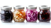 Assorted fermented vegetables in glass mason jars including black olives, pickled onions, red cabbage and berries arranged in row on white background.
