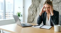 Stressed businesswoman with headache working at desk with laptop in modern office environment.