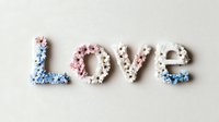 Word LOVE spelled with tiny delicate flowers in pink, blue and white on light neutral background, arranged in typography style. Romantic floral lettering composition.