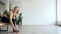 Young woman with blonde hair and fair complexion stretching before workout in bright studio space with plants and natural light for fitness and wellness content.