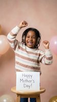 Happy African American girl with headphones dancing while holding Mother's Day card, celebrating with joy and excitement in pink studio setting.