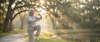 Senior Asian woman practicing tai chi in peaceful park during golden hour morning exercise routine for health and wellness.