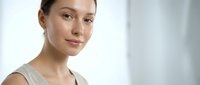 Young woman with fair skin and light brown hair wearing a neutral beige sleeveless top, looking at camera with calm expression in bright studio setting for skincare, wellness and beauty campaigns.