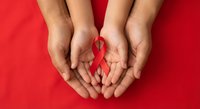 Hands holding red ribbon symbol for AIDS awareness, HIV prevention campaign, health support and solidarity concept on red background.