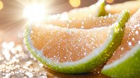 Fresh lime wedges with salt crystals and sunlight flare creating bright bokeh effect, macro food photography for cocktail and beverage concepts.