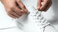 Male hands tying white laces on a clean white sneaker, close-up shot highlighting minimalist style and everyday casual footwear routine.
