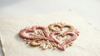 Delicate embroidered heart with pink and gold threads on cream fabric, showcasing traditional needlework and romantic handicraft artistry.