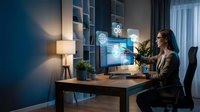Professional businesswoman working late at modern home office desk with computer displaying global network connections and digital interface graphics.