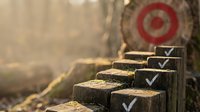Wooden steps with white checkmarks leading toward a red target bullseye, symbolizing progress, achievement, and goal completion in business strategy and success planning.