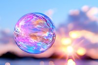 Iridescent soap bubble floating in sunset sky with bokeh lights, showcasing rainbow colors and reflective surface against blurred nature background.