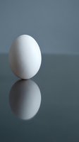 White egg standing upright on reflective surface with mirror reflection against gray background for minimalist design concepts.