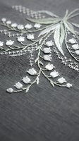Delicate white floral embroidery with green stems on gray fabric showcasing intricate needlework and botanical motifs for textile and craft projects.