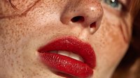 Close-up portrait of young woman with freckles wearing glossy red lipstick. Natural beauty and makeup concept for cosmetics advertising.