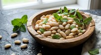 Fresh white beans in rustic wooden bowl with mint leaves on dark stone surface. Healthy legumes protein source for cooking and nutrition concepts.