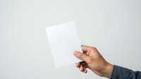 Hand holding blank white card or paper against neutral background, suitable for mockups, branding, and promotional designs.