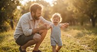 Father and toddler son enjoying quality time together in sunny park during golden hour. Happy family bonding moment with warm natural lighting.