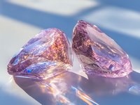 Raw pink crystal gems with rainbow light reflections on white surface against blue sky background, showcasing natural mineral formation and optical properties.