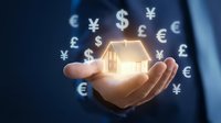 Businessman holding glowing house icon with floating currency symbols representing real estate investment and global property finance opportunities.
