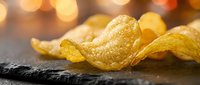Golden crispy potato chips on dark slate surface with warm bokeh lights creating cozy snack atmosphere for food photography and culinary designs.