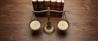 Brass scales of justice with law books on wooden desk representing legal system, courtroom, attorney office, judicial balance and legal profession.