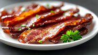 Crispy fried bacon strips garnished with fresh parsley on white ceramic plate, close-up view showing texture and caramelization of cooked meat.